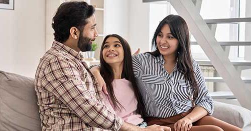 An image of a girl sitting on the sofa with her mother and father and looking up smiling at her father. 