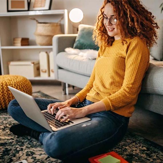 A high school student in a yellow sweater sitting down with a laptop